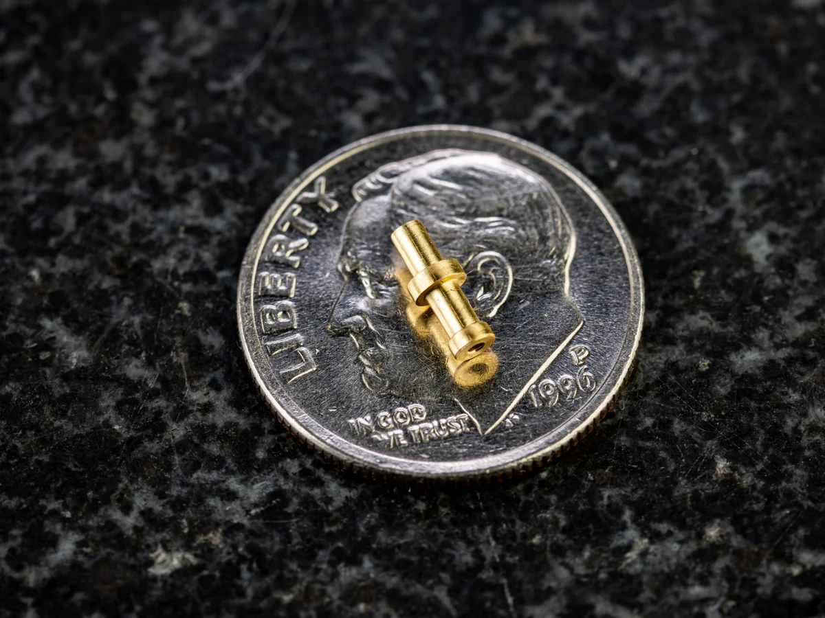 Miniature Swiss-turned brass component on a dime for scale machined on Tsugami Swiss-type lathe